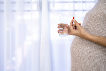 Portrait of pregnant woman standing near window with white curtain.Pregnancy take drug or vitamin...