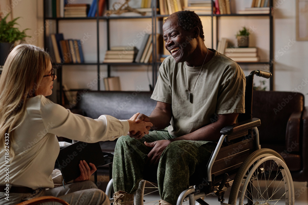 Wall mural joyful black veteran with disability shaking hand of his female therapist after successful session