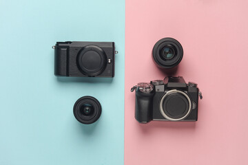Two modern mirrorless cameras with a lens on a blue pink background. Top view