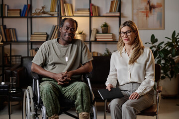 Female psychologist and senior black soldier in wheelchair sitting in office looking at camera