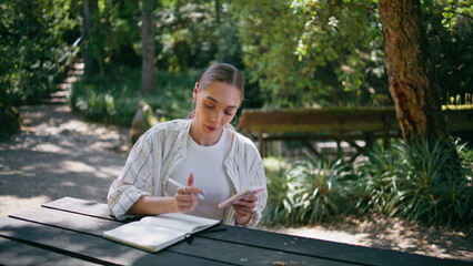 Fototapeta premium Girl writer noting information to copybook from smartphone in forest close up.
