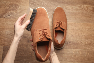 Hands cleaning suede shoes with a brush on wooden floor. Top view. Shoe care