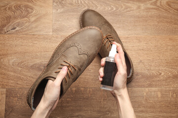 Hands apply water-repellent spray to shoes on floor. Top view. Shoe care