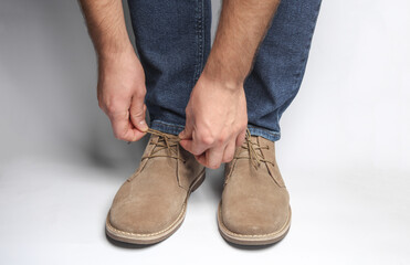 Man tying laces of suede shoes on white background