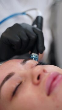 Professional aesthetician performs hydrafacial on client in spa. Hydro dermabrasion device rejuvenates skin, improves texture. Woman enjoys anti-aging treatment, skincare boost in clinic.