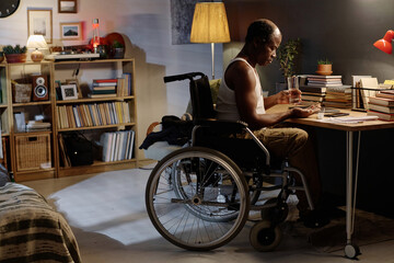 Black man in wheelchair examining handful of pills in his palm sitting in his bedroom at home
