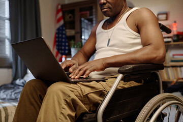 Fototapeta na wymiar Senior black man with physical disability typing on his laptop keyboard working remotely from home