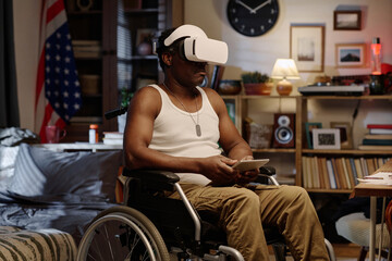 Black man with physical disability wearing VR headset while sitting in his apartment