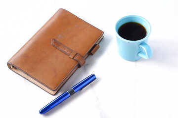 コーヒーを飲みながら、茶色の革のシステム手帳でデスクワークをしているイメージ
