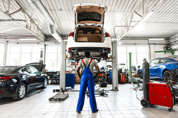 Fototapeta premium Pensive young African mechanic in car service looking at car thinking of how to repair it
