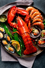 Big red lobster on plate with shrimp and mussels with lemon, souce pesto and bread. Seafood concept