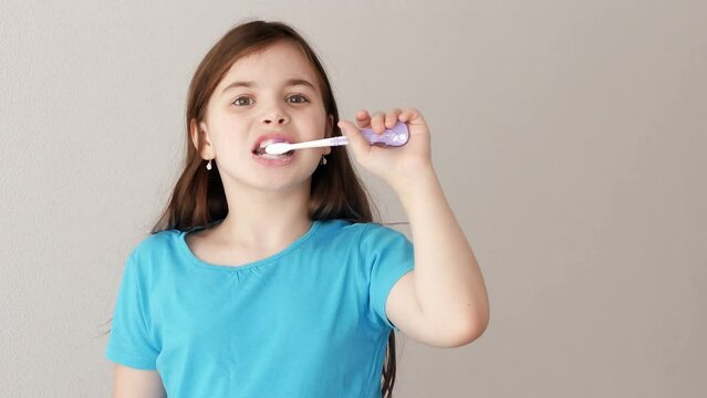 A little smiling girl with a blue T-shirt is brushing her teeth with a toothbrush with toothpaste. Oral hygiene and caries prevention.