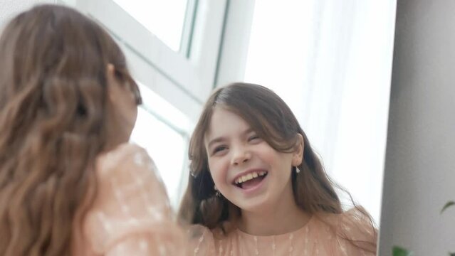 A pretty little girl grimaces in front of the mirror, smiles broadly, straightens her hair, and rolls her eyes in fright. Valentine's Day concert.