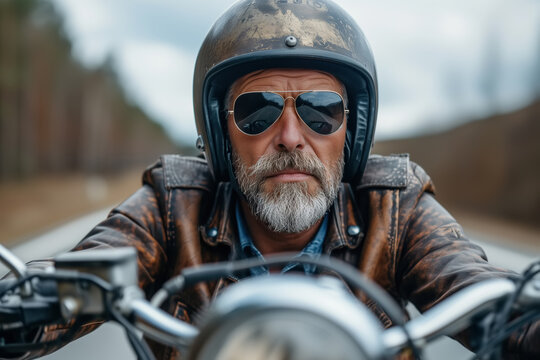 Portrait of a bucker on a motorcycle riding along road, a brutal handsome middle-aged man driver in a leather biker jacket and glasses
