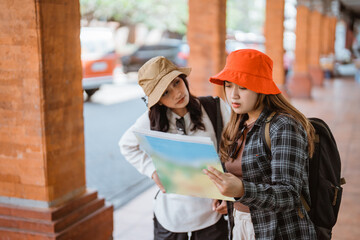 two attractive girls look at a map and chat while getting to a tourist destination