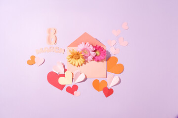 An envelope containing several flowers in different colors. Many paper hearts decorated with the word March 8 made of paper. International Women's Day is now celebrated in over 100 countries