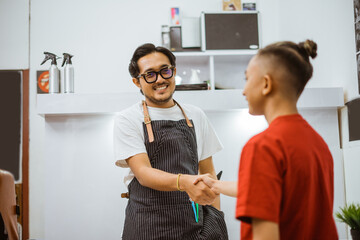 asian male barber greeting his young client with friendly expression hand shake gesture