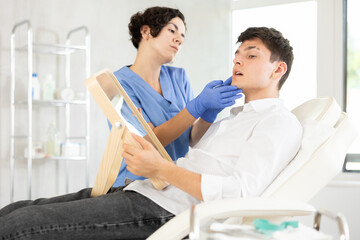 Beautician woman using mirror consulting young man in clinic