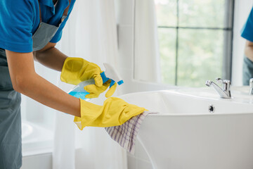A maid wearing gloves diligently cleans bathroom sink and faucet eliminating limescale with spray...