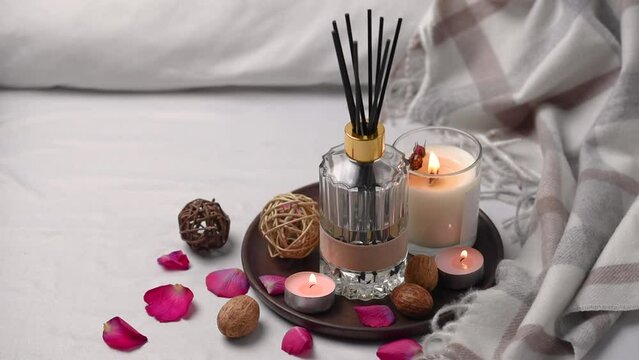 Aroma scented reed diffuser glass is on the tray with scented candle on the bed