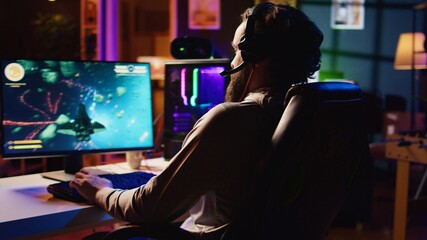 Man at home playing singleplayer videogame with spaceship shooting laser beams at asteroids,...