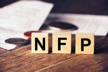 Word "NFP" on cube dice lay on wood table with bill and coin on background , US economic calendar concept.