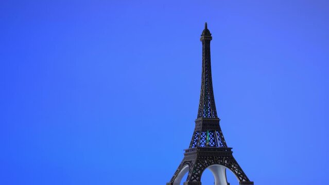 Rotating  the Eiffel Tower against a blue background. Miniature replica of the Eiffel Tower rotating against a blue background. Paris 2024 Summer Olympics.