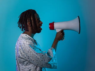 African American man dons traditional attire, passionately utilizing a megaphone against a striking blue background, symbolizing his vocal and cultural empowerment in the pursuit of social justice and