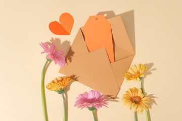 Brown envelope containing a piece of paper in orange color with a paper heart placed next to it. Branches of flowers decorated below. International Women's Day is celebrated on March 8 every year