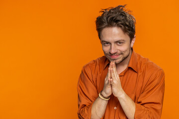 Sneaky cunning Caucasian young man with tricky face gesticulating and scheming evil plan, thinking over devious villain idea, cheats, jokes pranks. Guy isolated on orange studio background. Copy-space - obrazy, fototapety, plakaty