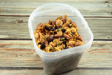 Pile of caramel cornflake mixed with baked cashew nut, almond, raisin and pumpkin seed in the plastic container. Mock up of sweet snack product.
