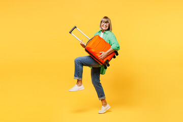 Traveler elderly woman wear green casual clothes hold suitcase pov guitar isolated on plain yellow background. Tourist travel abroad in free spare time rest getaway. Air flight trip journey concept.