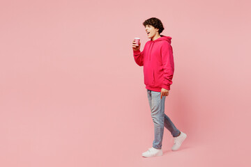 Fototapeta na wymiar Full body side view young Caucasian man wears hoody casual clothes hold takeaway delivery craft paper brown cup coffee to go isolated on plain pastel light pink background studio. Lifestyle concept.