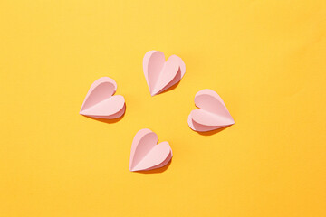 Pastel pink paper hearts are artistically arranged on a yellow background. The space is viewed from above with a women's day theme. Banner, commercial.
