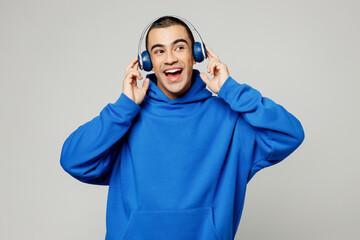 Young smiling happy middle eastern man he wear blue hoody casual clothes listen to music in headphones look aside on area isolated on plain solid white background studio portrait. Lifestyle concept.