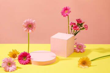 Front view of two pastel pink podiums decorated with gerberas and carnations on a yellow pink background. Ideal space for product display. Women's Day theme.