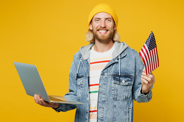 Young happy blond IT man he wear denim shirt hoody beanie hat casual clothes hold American flag use...