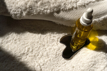 a bottle of oil and a stainless steel gua sha scraper lie on a towel