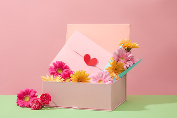 Fresh flowers and a pastel pink envelope inside a gift box. Prepare women's day gifts. Copy space with front view. Holiday theme, banner, advertising.