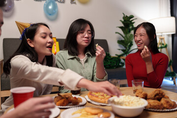 Group of happy young friends celebrating at a party with snacks popcorn pizza and drinks. The atmosphere at the event was full of laughter while sitting at the dining table together in the home office