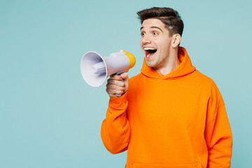 Young man wear orange hoody casual clothes hold in hand megaphone scream announces discounts sale Hurry up isolated on plain pastel light blue cyan color background studio portrait. Lifestyle concept