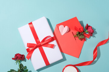 A gift box with red ribbon decorated with a red envelope containing rose and a paper heart. A roll of red ribbon featured. International Women's Day has since grown worldwide