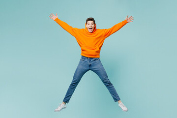 Fototapeta na wymiar Full body young excited fun man wears orange hoody casual clothes jump high with outstretched arms hands isolated on plain pastel light blue cyan color background studio portrait. Lifestyle concept