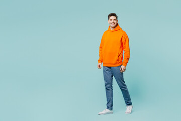 Full body smiling happy cheerful young man he wears orange hoody casual clothes look camera walking...
