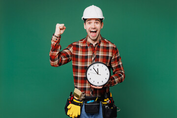 Young employee laborer man wear red shirt hardhat hat work hold clock do winner gesture isolated on...