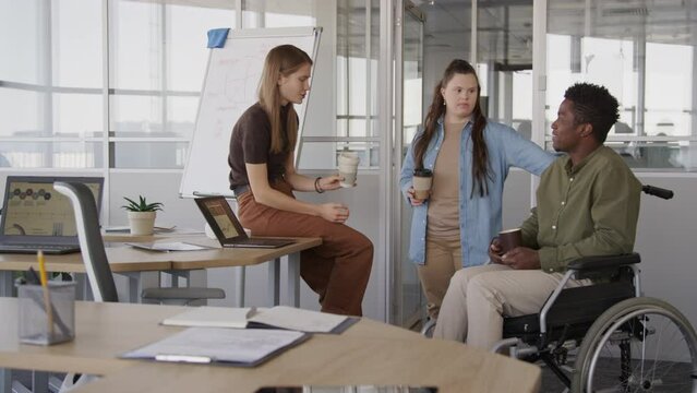 Medium shot of three diverse young male and female office colleagues having conversation during coffee break at workplace