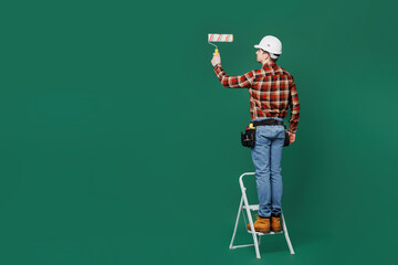 Full body young employee handyman man wears red shirt hardhat stand on stepladder paint hold roller...