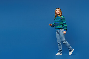 Full body side profile view young smiling happy woman she wear knitted sweater casual clothes walking going look camera isolated on plain blue cyan color background studio portrait. Lifestyle concept