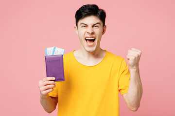 Traveler man wear yellow casual clothes hold passport ticket do winner gesture isolated on plain pink background Tourist travel abroad in free spare time rest getaway. Air flight trip journey concept