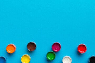 jars with gouache of different colors on Colored background. hobby painting. Top view with empty space. workplace for creativity. home teaching concept drawing